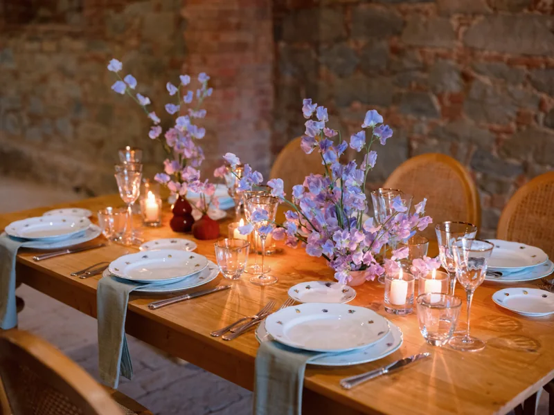 Fiori lilla e candele sulla tavola in legno, accanto alle pareti in pietra