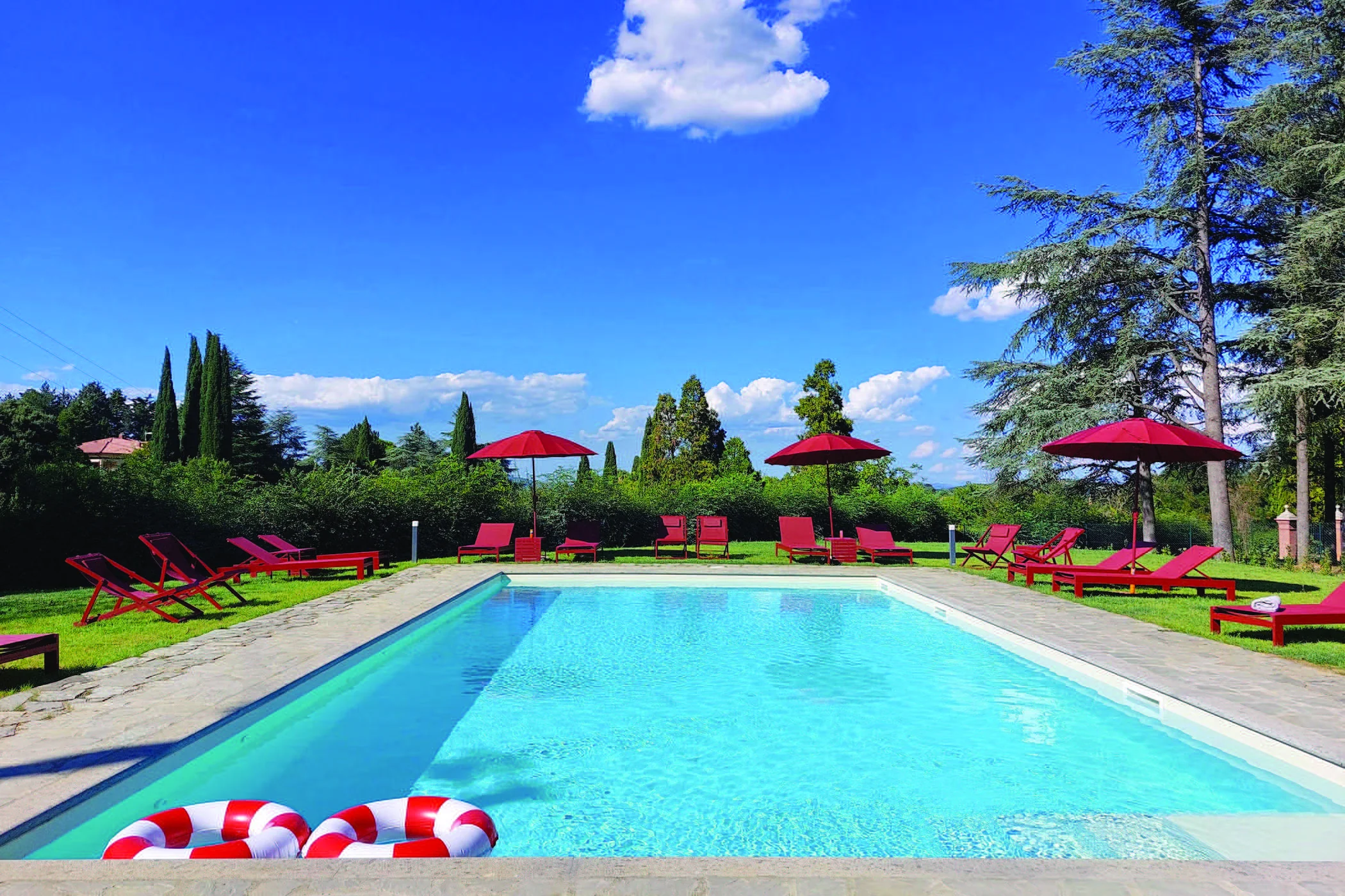 La piscina all’aperto di The Monteleone, circondata dal giardino, con lettini e ombrelloni rossi